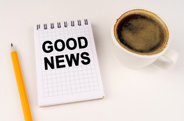 On a white surface, a cup of coffee, a pencil and a notepad with the inscription - GOOD NEWS