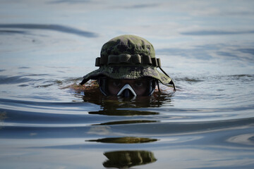 Military diver in a diving mask and a camouflage panama hat in the water at sea.