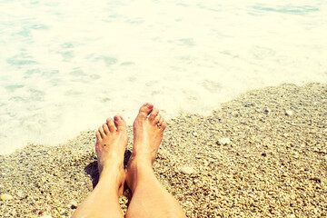Women's bare feet on a pebble beach near the sea on a sunny day. Vacation background	
