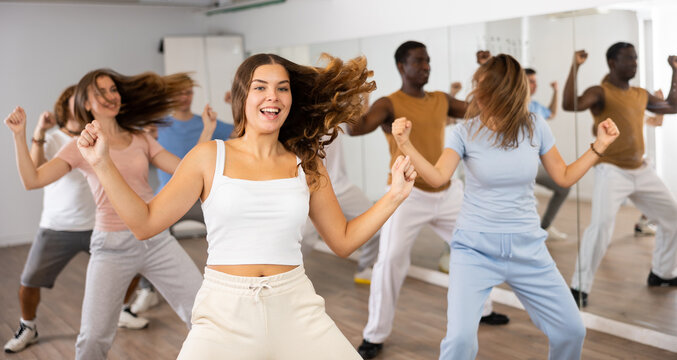 Group of excited young adult diverse dancers performing dynamic movements during training together in fitness studio
