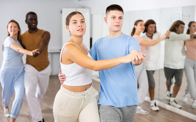 Smiling multiracial men and women enjoying partner dance while training together in modern studio