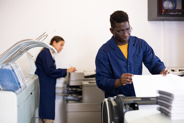 Focused African American male in a blue robe uniform using plotter during workflow in the typography