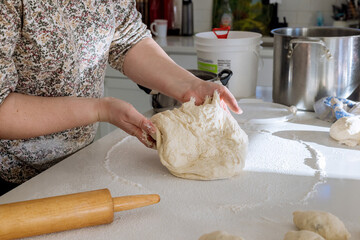 Yeast dough is being mixed on white countertop by woman for making homemade donuts