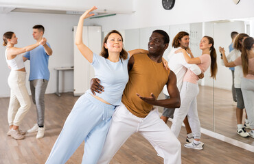 Joyful young adult couples learning passionate pair dancing during practicing in choreography class