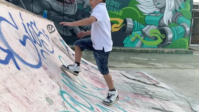 Cute Preschool Boy Running Up The Ramp In The Skate Park And Trying To Climb. Falling Down And Laughing In Slow Motion. High Quality FullHD Footage