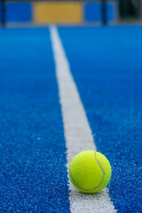 A paddle tennis ball in the foreground on the line of a blue paddle tennis court, racket sports concept