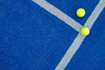 Two balls next to the lines of a paddle tennis court