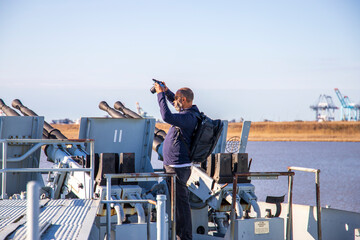 An African American man standing on the front of the USS Alabama taking pictures surrounded by the...