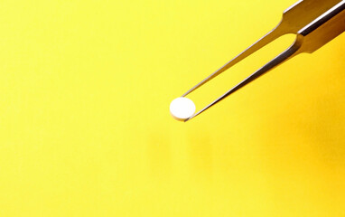 Thin tweezers taking a small white pill