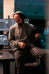 Young coder fooling around with keyboard playing guitar, working on user interface with multiple...