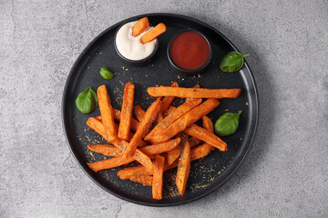 Sweet potato sticks in a black plate served with mayonnaise and ketchup sauce.