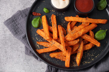 Sweet potato sticks in a black plate served with mayonnaise and ketchup sauce, top view. Vegetarian food and healthy eating concept.