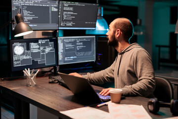 Software developer coding database on multiple monitors to program new server interface at night....