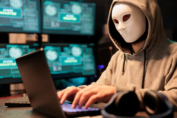 Cyber terrorist wearing mask and hood to hack computer system, breaking into company servers to steal big data. Masked man looking dangerous and scary, impostor creating security malware. - obrazy, fototapety, plakaty