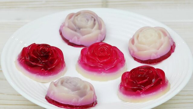 Rose shaped jelly dessert made from raspberries and cream in a white plate on a white wooden table.