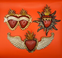 Three red and golden tin mexican hearts on red background