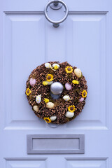 Blue wooden door with Easter wreath. Easter decoration with Easter eggs and flowers