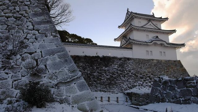 Slow pan over snow covered stone wall of historic Japanese castle at dawn