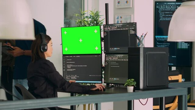 Asian system engineer programming app code on monitors with greenscreen template and terminal window. Asian coder working with chromakey template and isolated mockup on multiple screens.