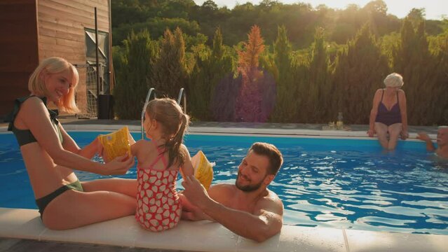 Parents putting on inflatable safety sleeves for swimming to their daughter
