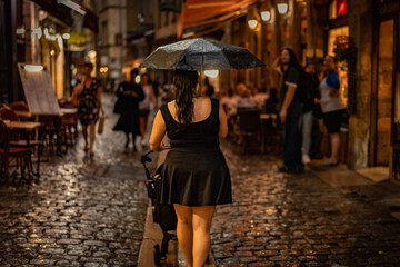 A woman pushing a stroller in the rain while walking down an alley in Lyon France