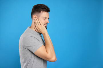 Young man suffering from ear pain on light blue background. Space for text