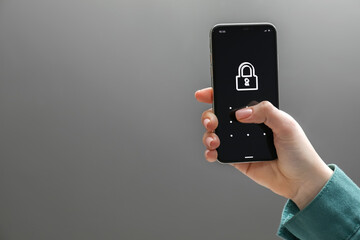 Woman unlocking smartphone with blocked screen on grey background, closeup. Space for text