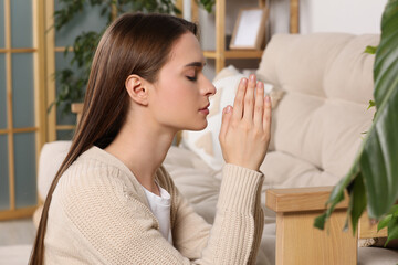 Woman with clasped hands praying at home