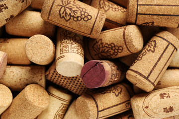 Many corks of wine bottles with grape images as background, top view