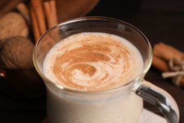 Glass cup of delicious eggnog on wooden table, closeup