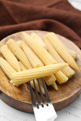 Pickled baby corn and fork on white wooden table, closeup