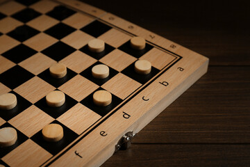 Checkerboard with game pieces on wooden table, closeup