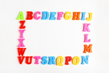 Frame of colorful magnetic letters on white background, flat lay with space for text. Alphabetic order