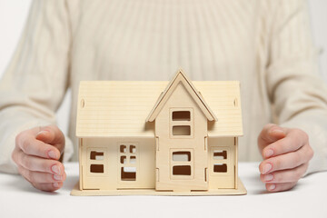 Home security concept. Woman with house model at white table, closeup