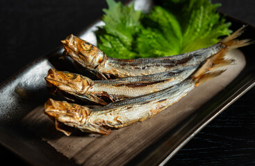 Grilled urume sardines on a black table. A side dish of sake.