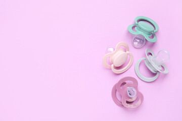 Flat lay composition with baby pacifiers on violet background. Space for text