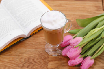 Glass of delicious cocoa, pink tulips and book on wooden table
