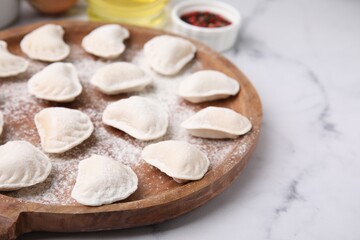 Fototapeta na wymiar Raw dumplings (varenyky) with tasty filling and flour on white marble table, closeup