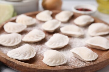 Fototapeta na wymiar Raw dumplings (varenyky) with tasty filling and flour on wooden board, closeup