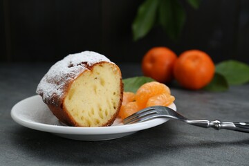 Piece of delicious homemade yogurt cake with powdered sugar and tangerines on gray table