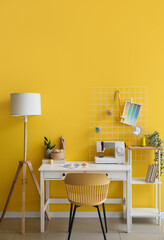 Tailor's workplace with shelving unit and lamp near yellow wall