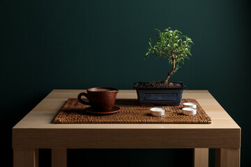 Table with Bonsai tree, cup of beverage and candles on dark background