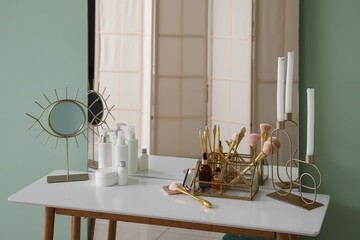 Table with cosmetics, brushes, candles and mirrors near green wall in makeup room