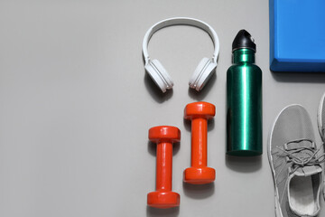 Sports water bottle with dumbbells, headphones and sneakers on grey background