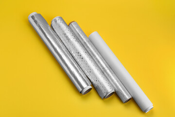 Naklejka premium Rolls of aluminium foil, baking paper and food film on yellow background