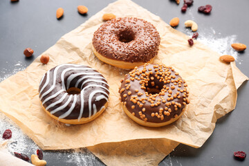 Sheet of baking paper with tasty donuts and nuts on dark background