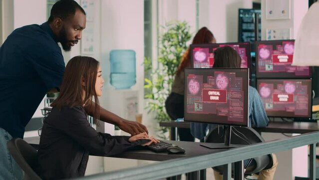 Diverse group of engineers having computer hacked and system crash on multiple monitors, reading critical error message flashing on screen. Security breach alert and hacking warning. Handheld shot.