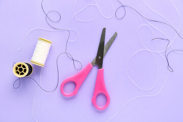 Thread spools and scissors on lilac background