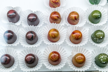 A chocolate confectionary and bakery glass display of handmade individual truffles in a variety of colors and flavors with white paper wrappers