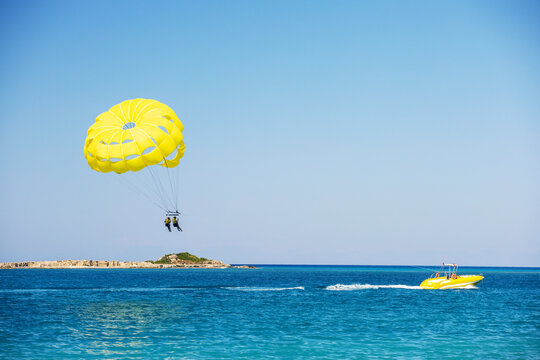 Parasailing above the ocean. Yellow parasail wing pulled by a boat. Sport activity on the beach.